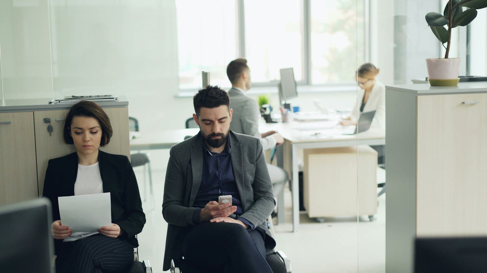 Two job candidates waiting on chairs in an open-plan office