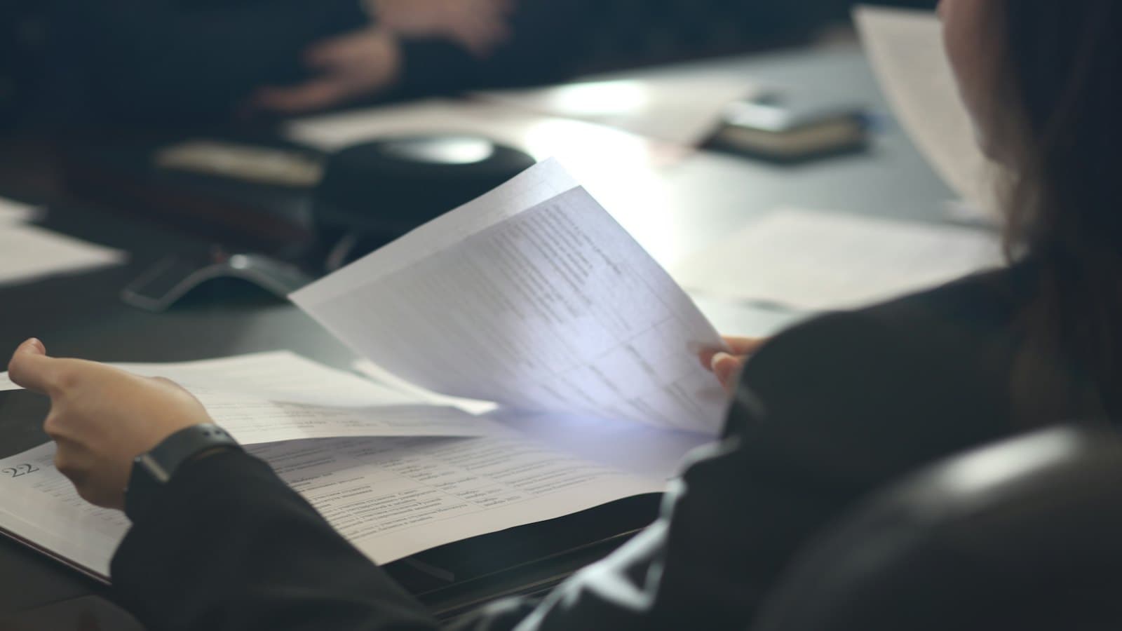 A person at a meeting table reading carefully through printed documents