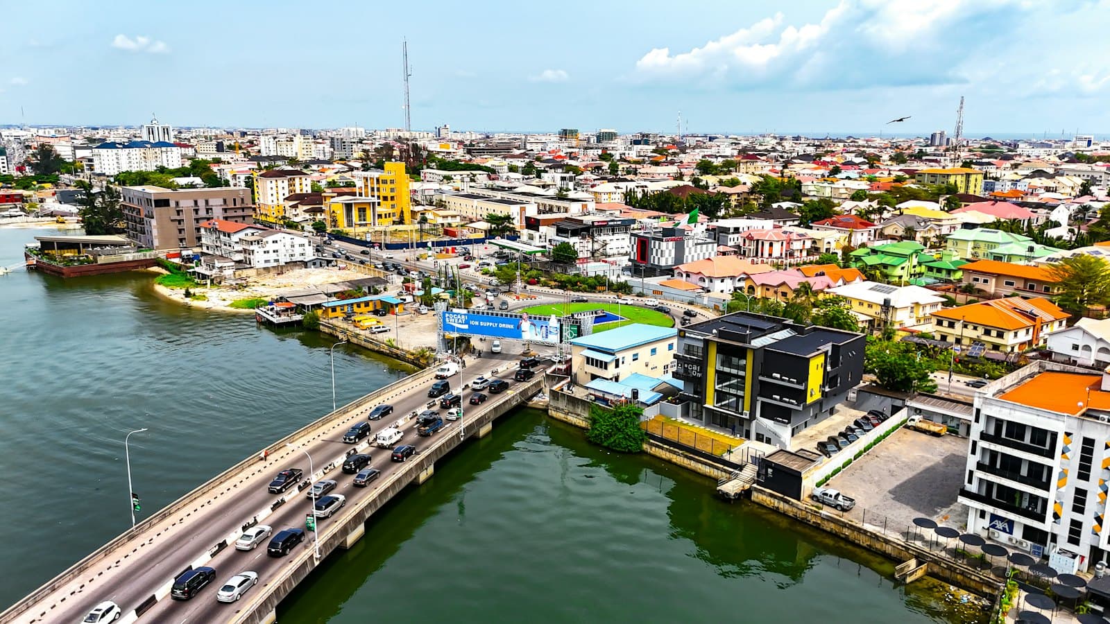 Aerial view of Lagos with traffic crossing a lagoon bridge and colourful rooftops