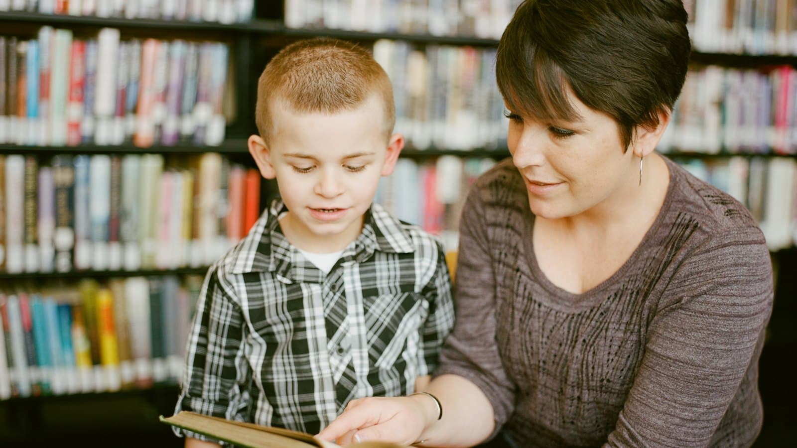 A woman and a young child reading a picture book together in a library