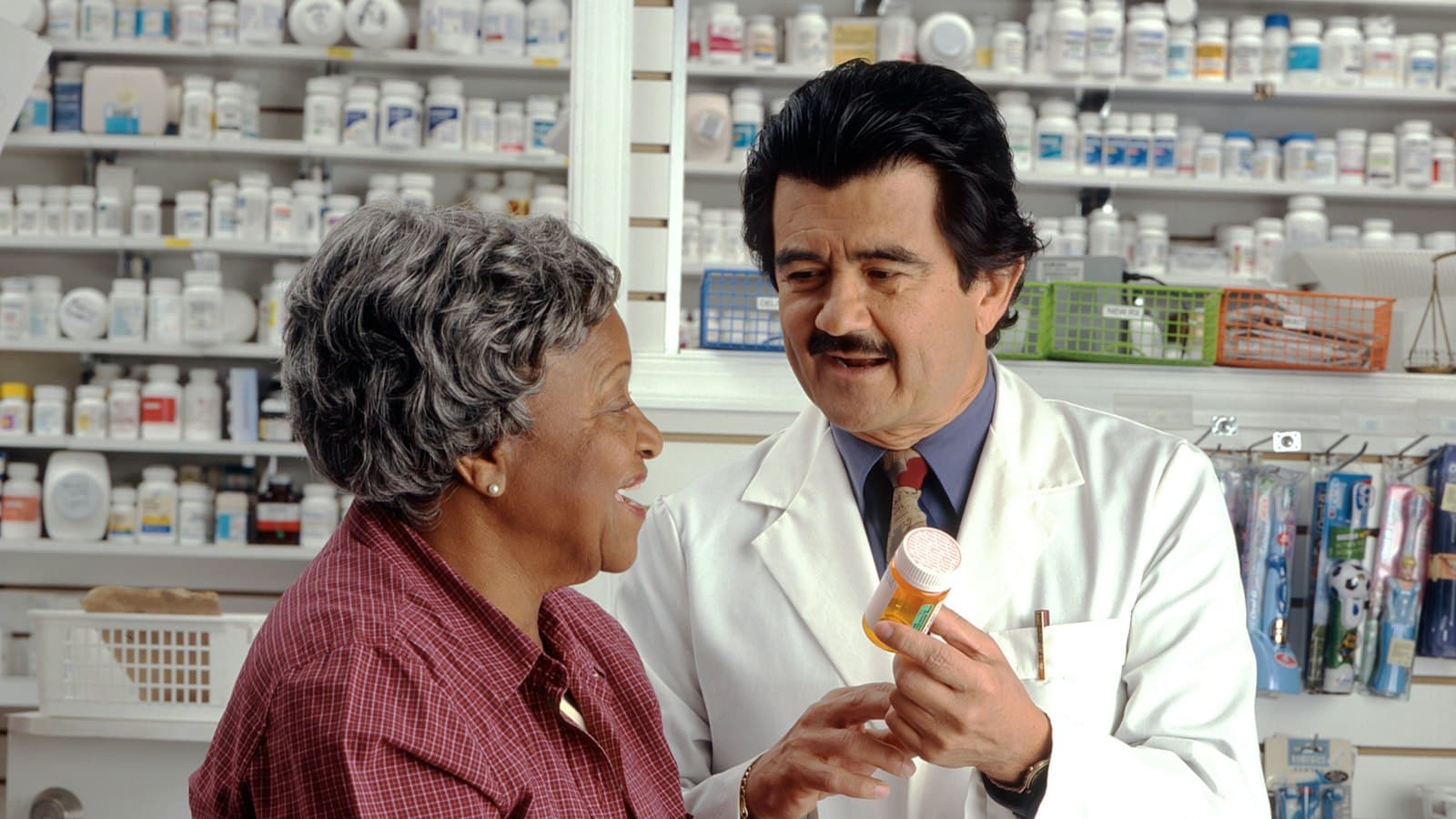 A pharmacist in a white coat showing a pill bottle to a woman