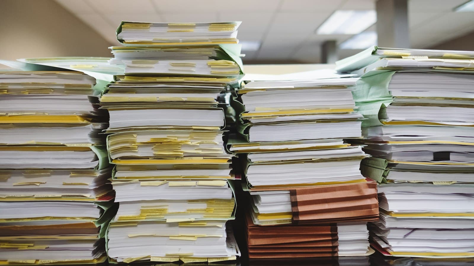 Tall stacks of paper case files and folders with yellow tabs piled up in an office