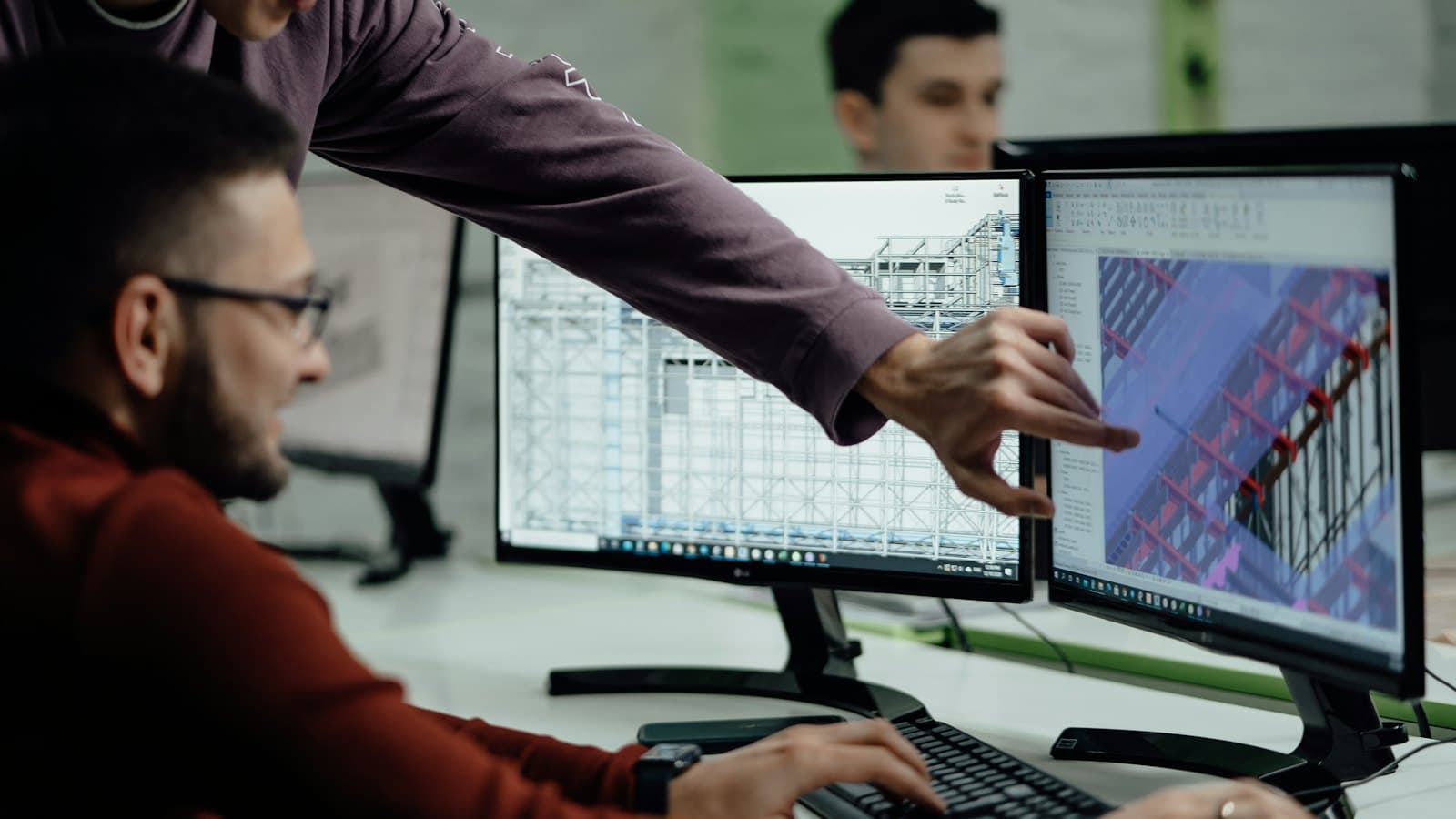 Engineers reviewing a 3D model on two computer monitors in an office