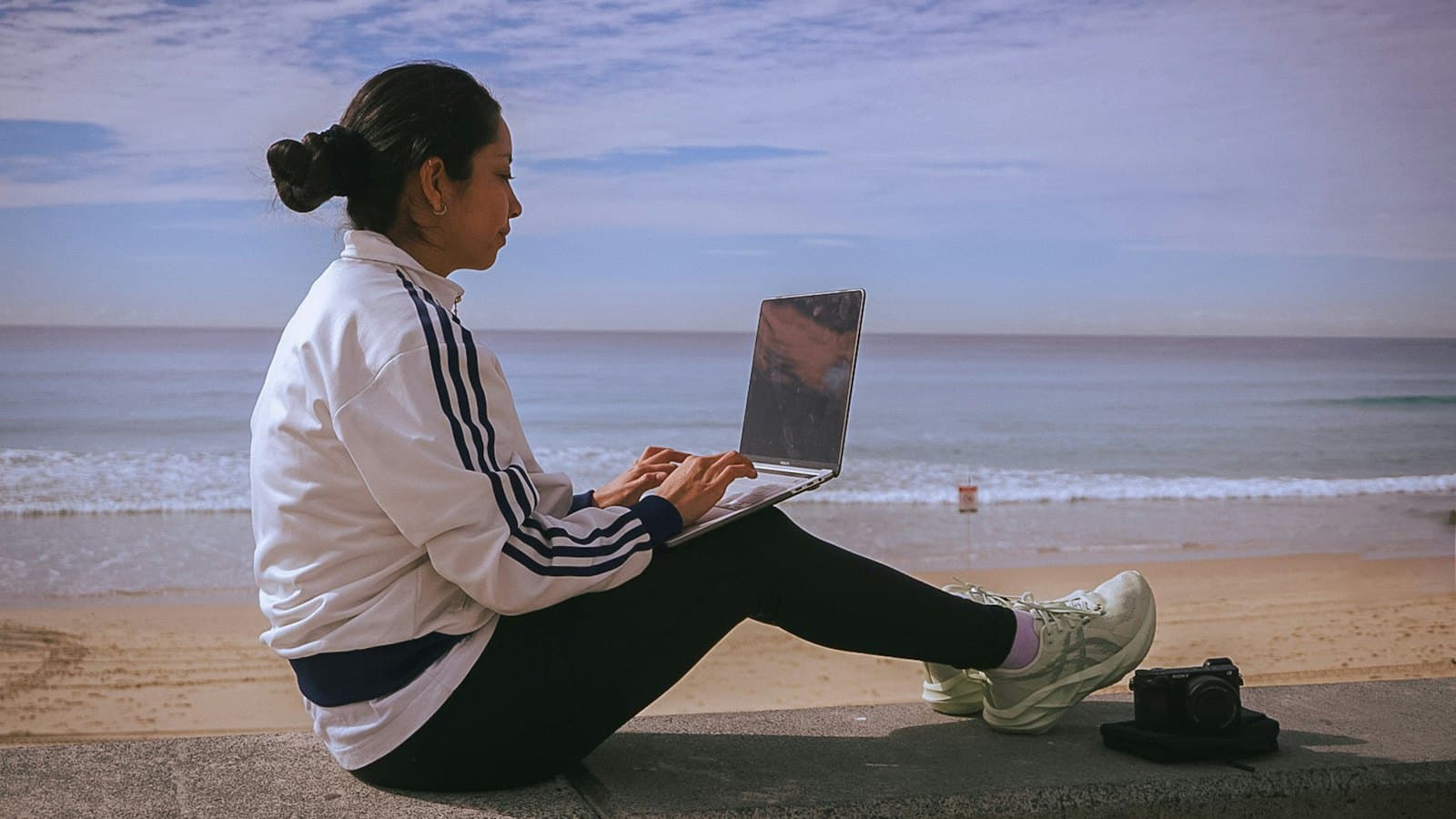 A woman working on her laptop at a table beside the beach