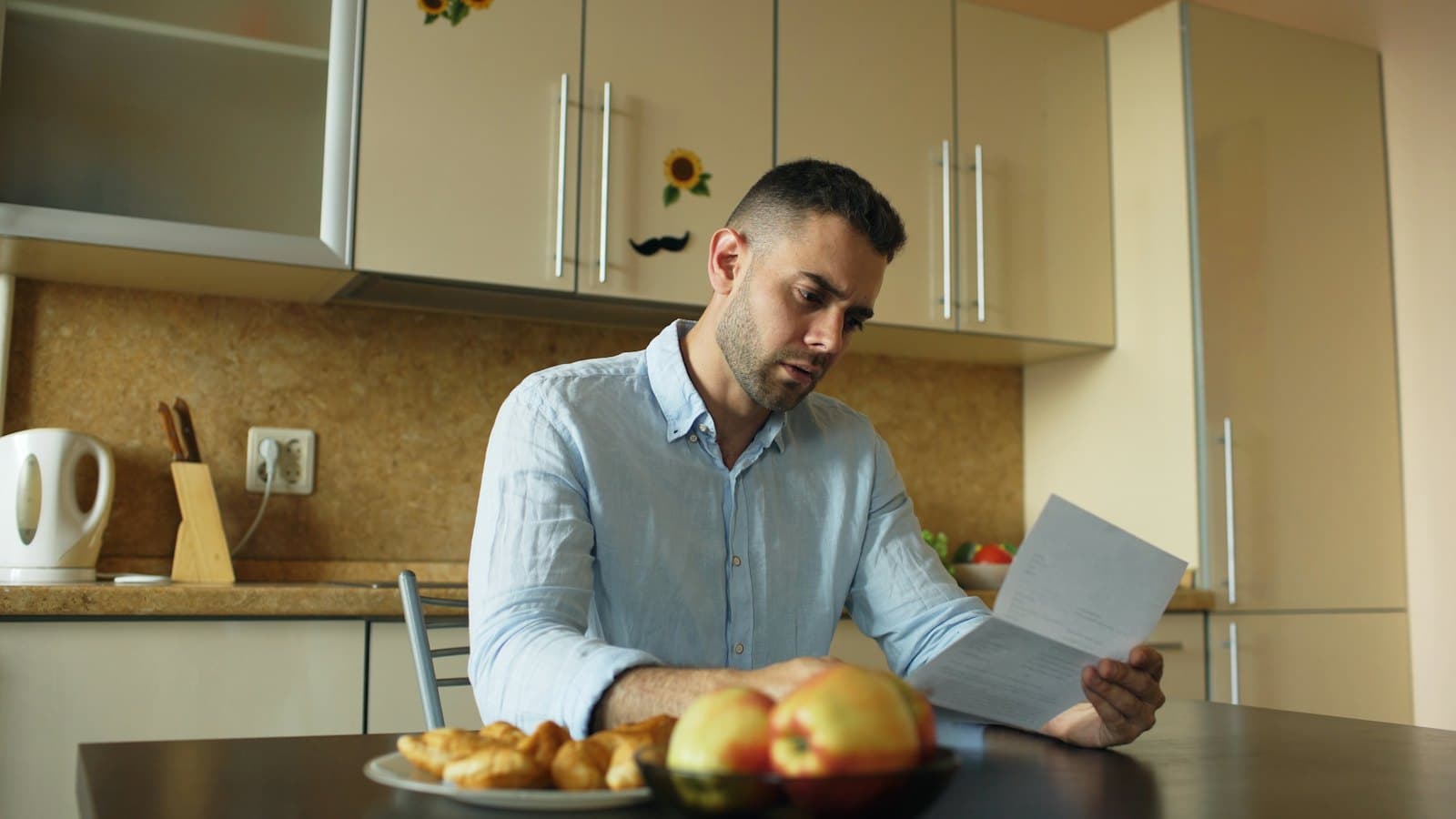 A man sits at a kitchen table reading through a letter and papers