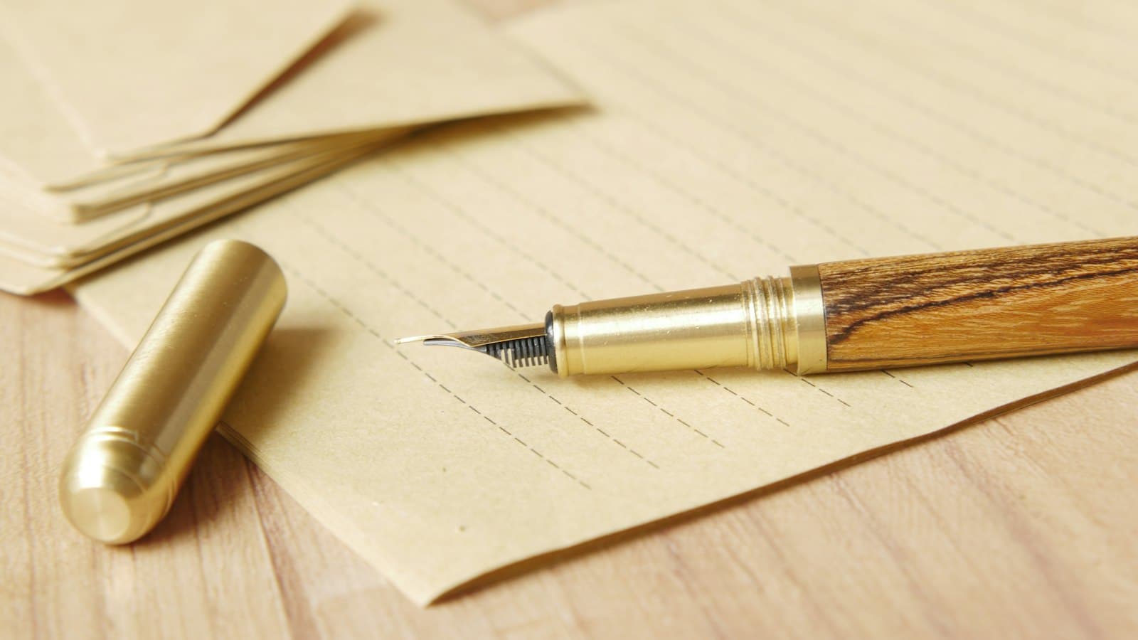 A wooden fountain pen and brass cap resting on lined writing paper