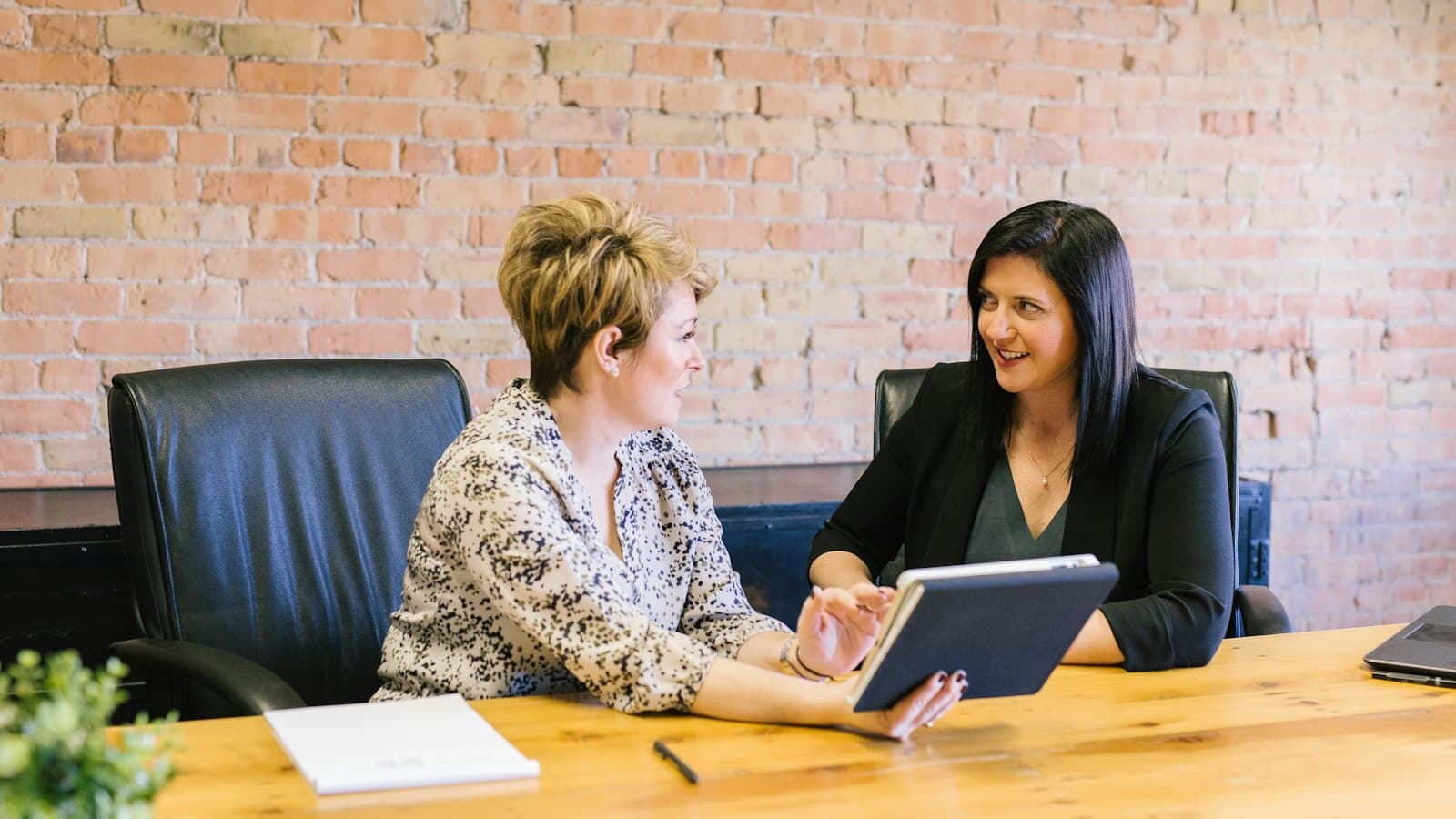 Two women sitting in leather chairs talking during an office consultation