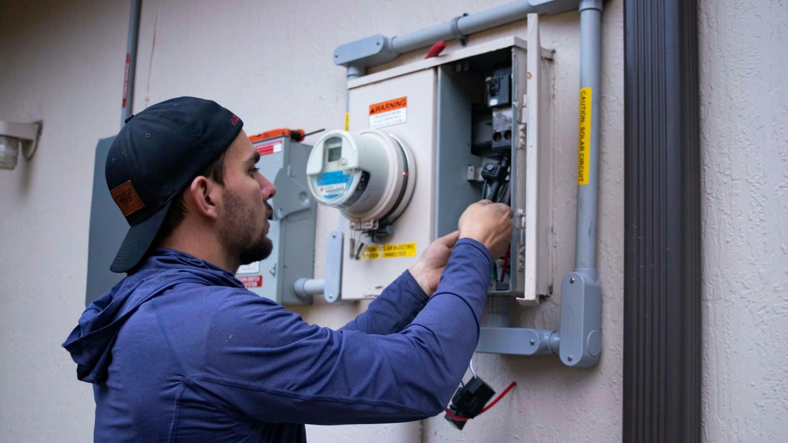 Electrician in a cap working on an outdoor electrical meter box
