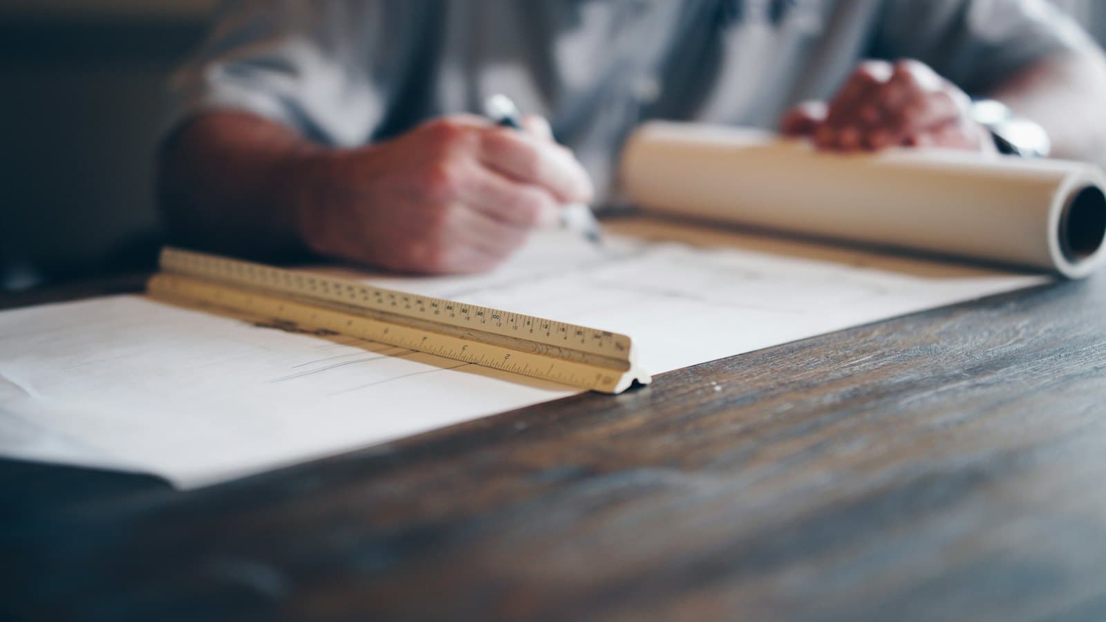 A person drafting plans on a long sheet of paper beside a scale ruler