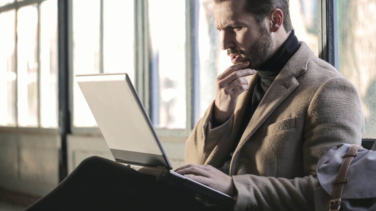 Man resting his chin on his hand while reading something on a laptop