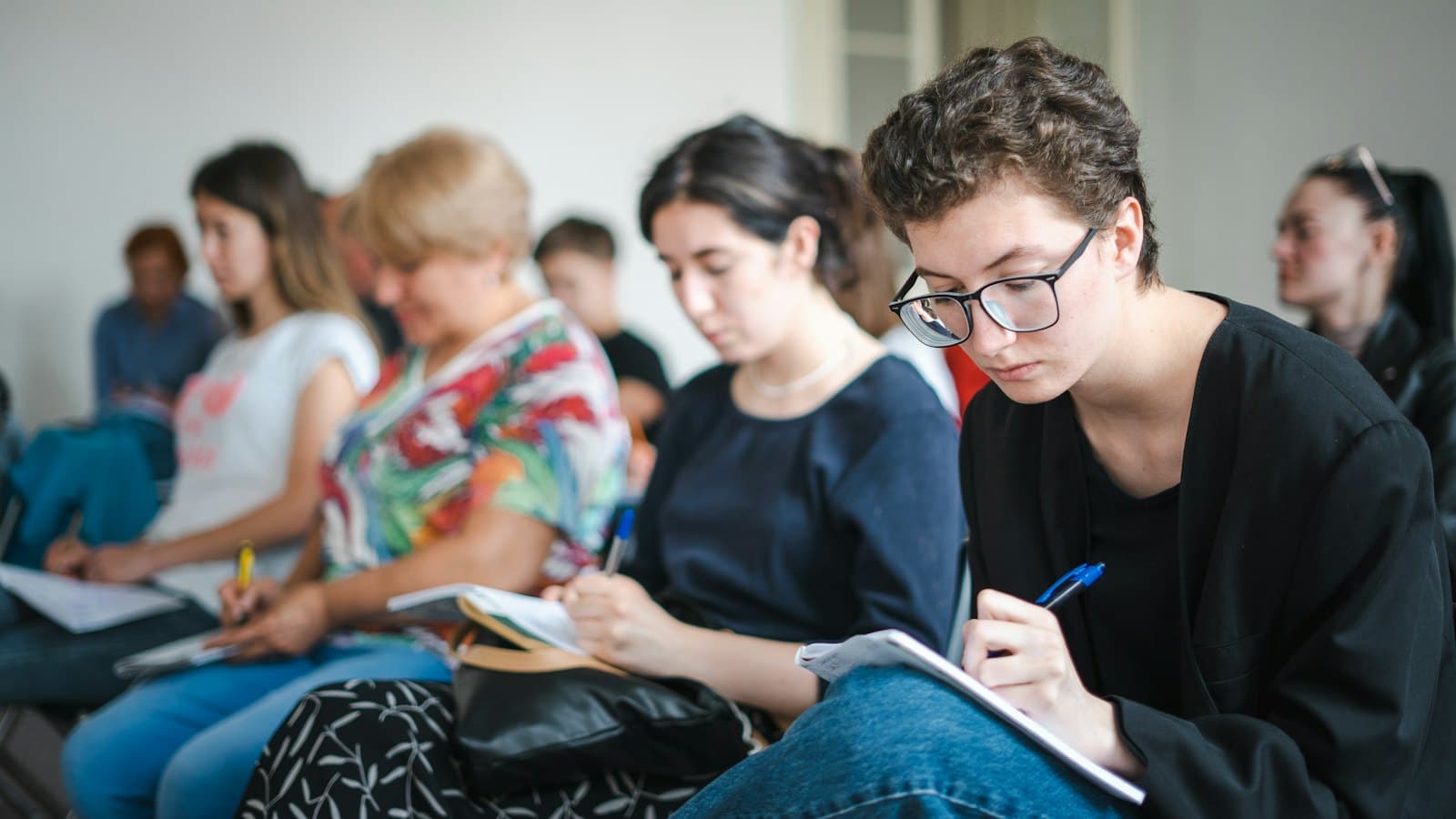 Adults seated in a classroom writing answers in notebooks during a class