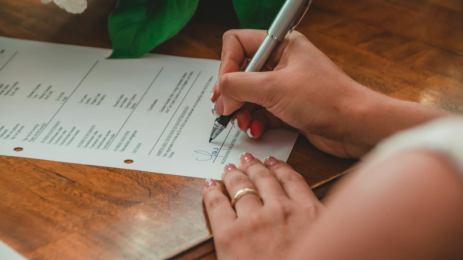 A woman signing an official printed form with a silver pen at a wooden table