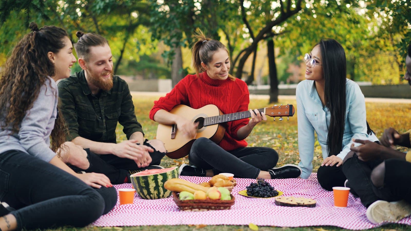 Friends enjoying a picnic together in a park while one plays guitar