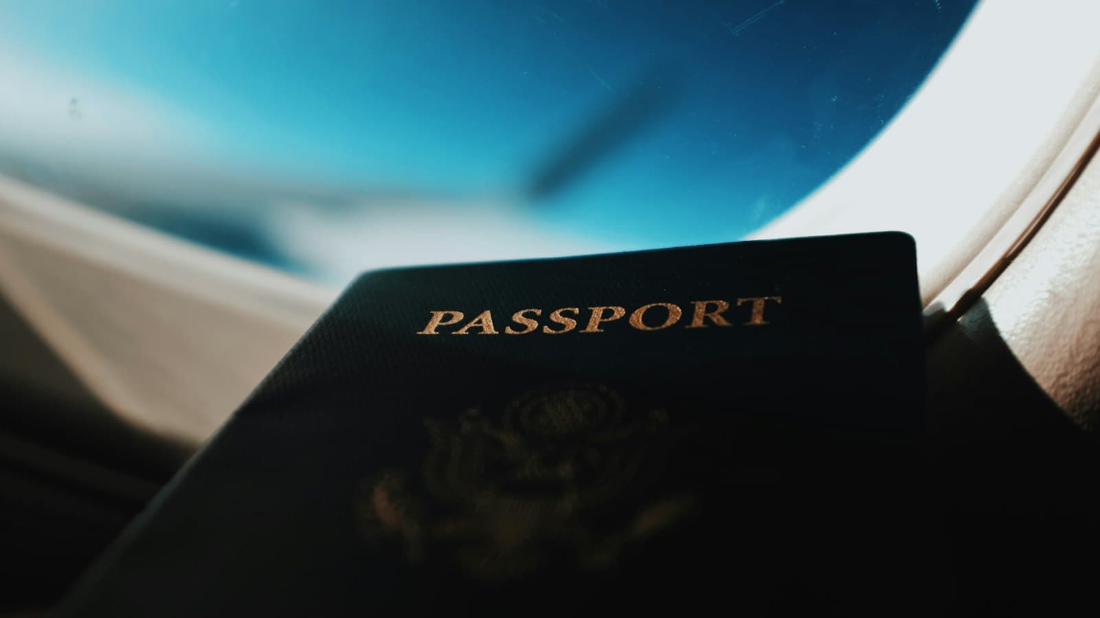 A passport held near an airplane window with blue sky beyond