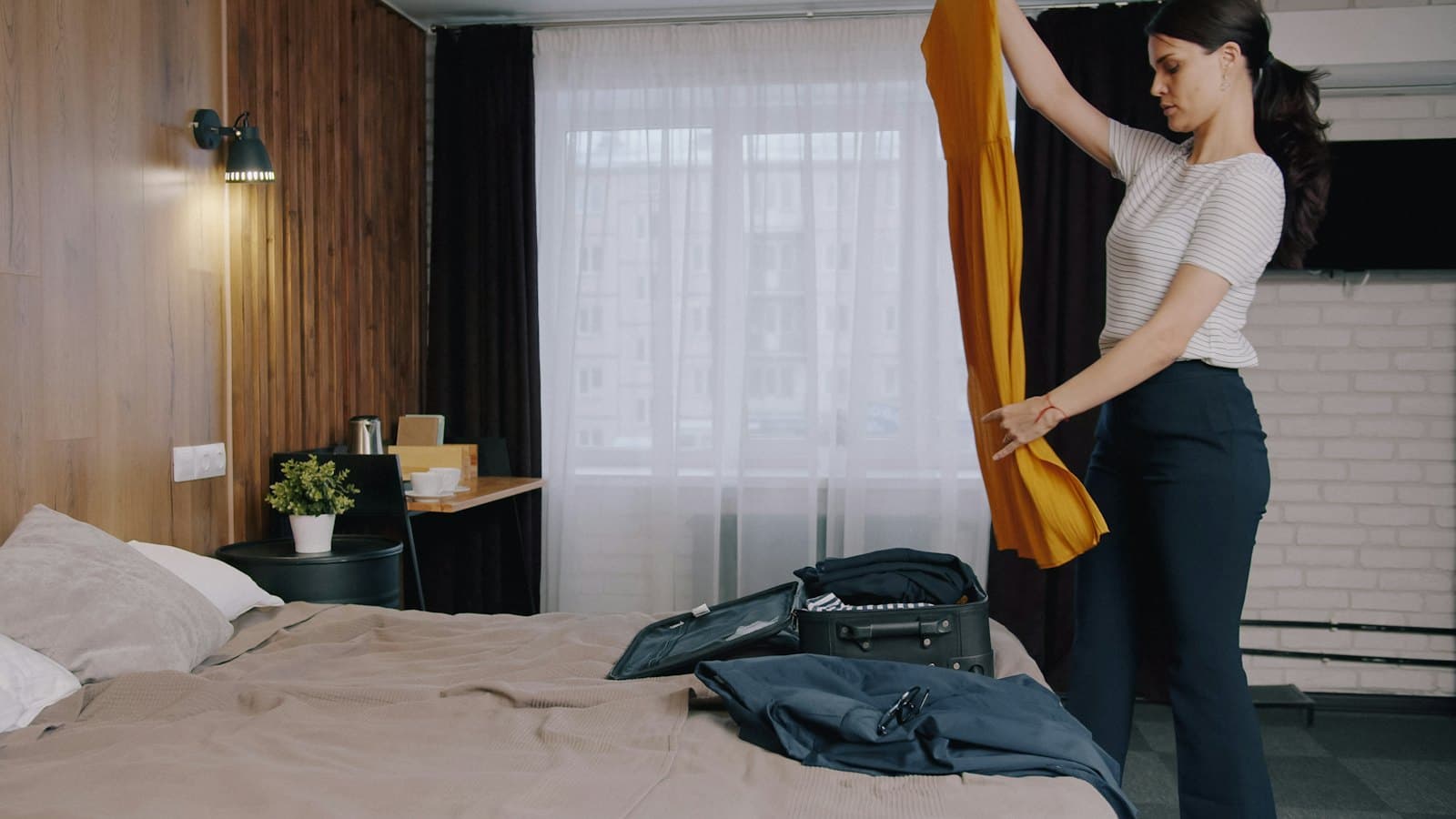 Woman holding up a yellow dress while packing a suitcase on her bed