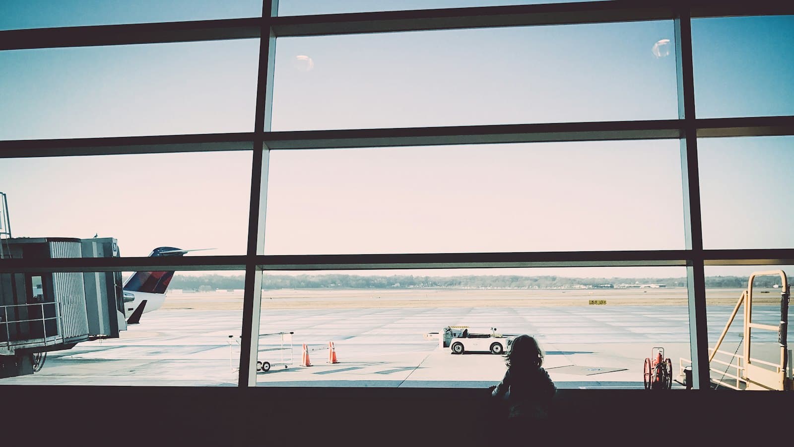 A small child gazing through a wide airport terminal window at the tarmac