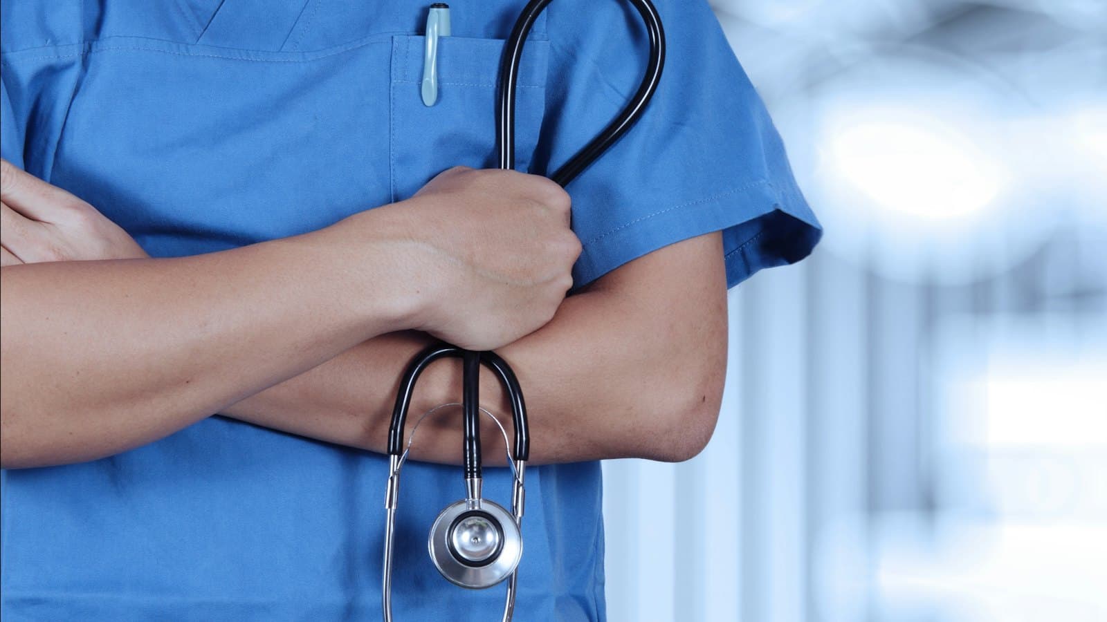 A healthcare worker in scrubs with a stethoscope draped over their arm
