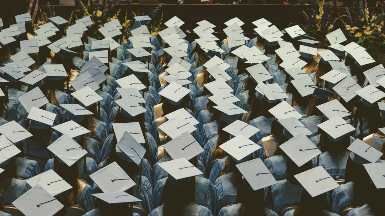 A large group of graduates in light blue gowns and caps at a ceremony