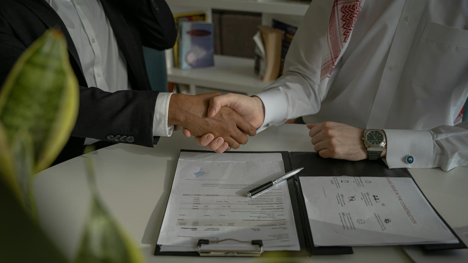 Two people shaking hands across a desk over a signed document