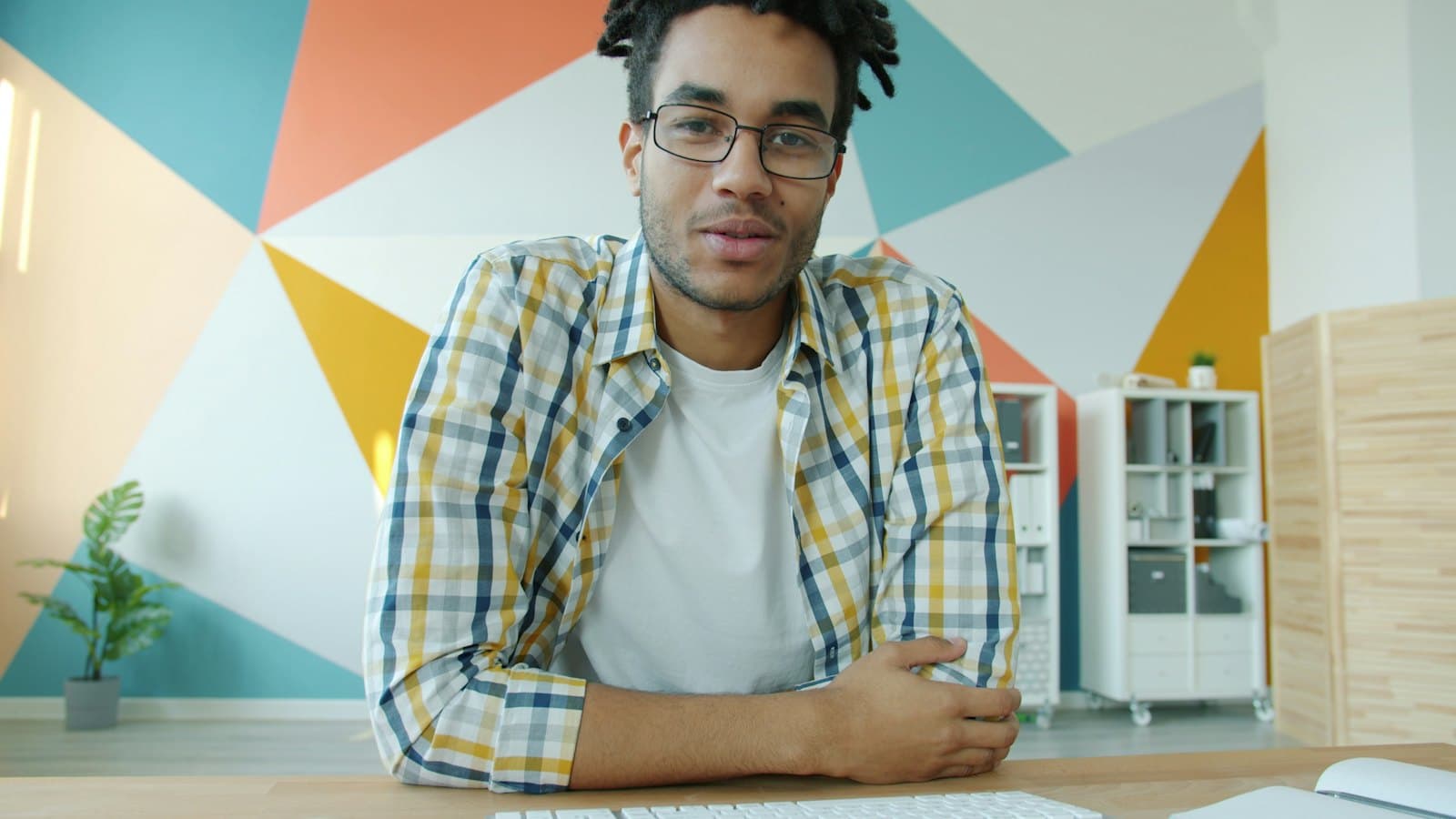 Man in glasses speaking on a video call at his desk in a brightly painted home office