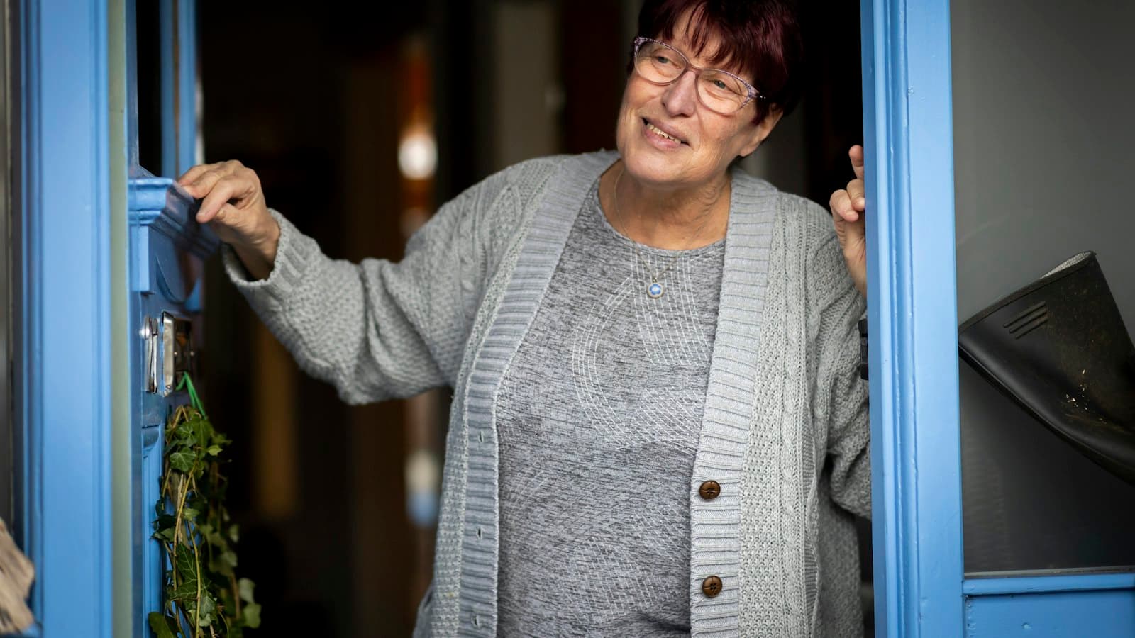 A smiling older woman standing in the open doorway of a blue front door