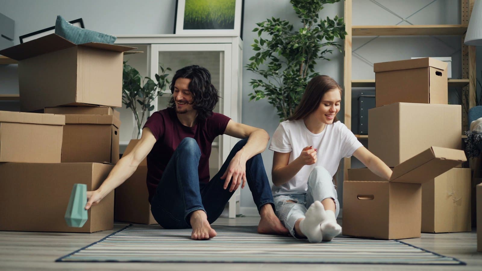 Couple sitting on a rug among cardboard boxes while packing up their home