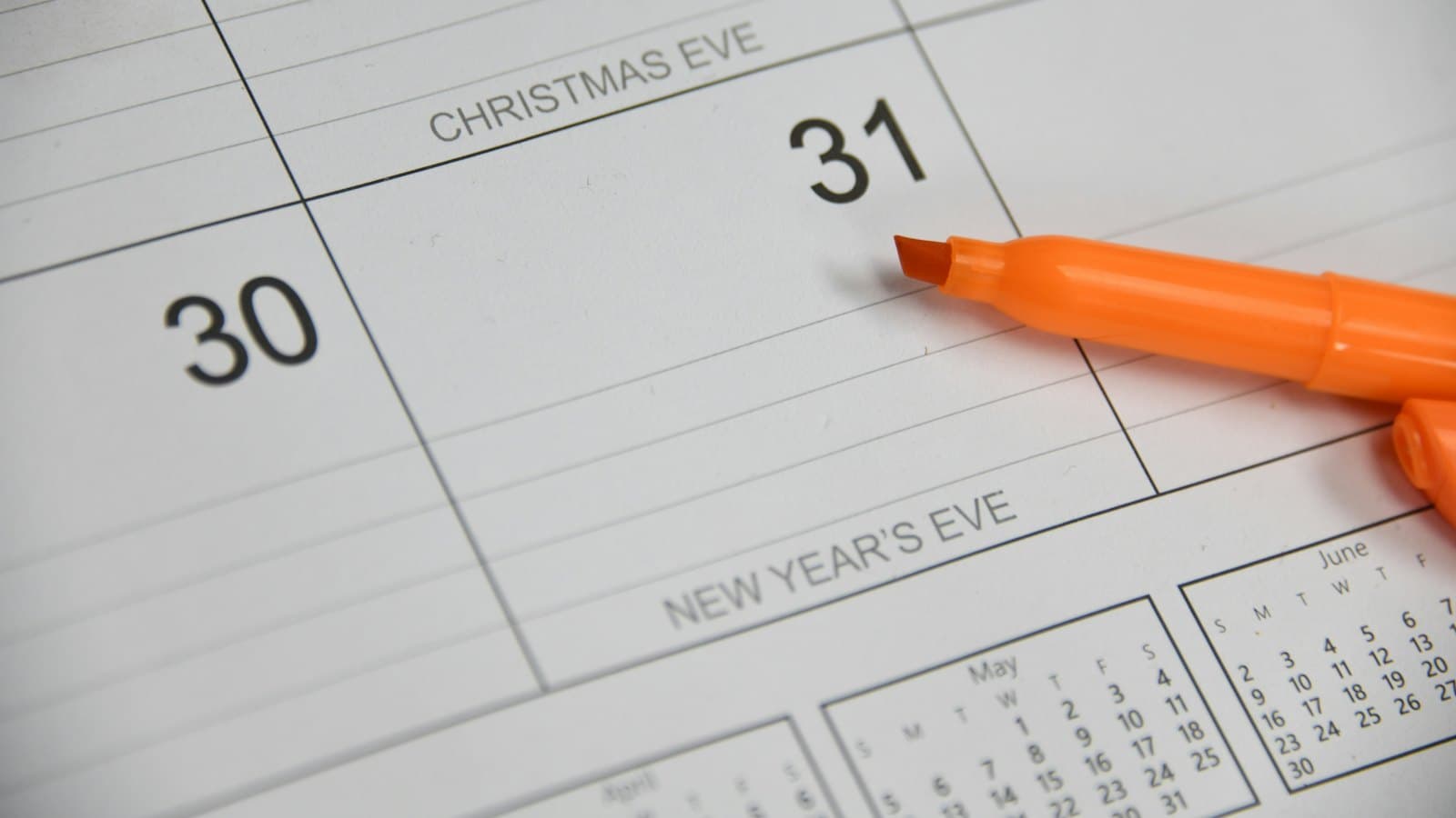 An orange highlighter pen resting on a paper calendar used to count travel days