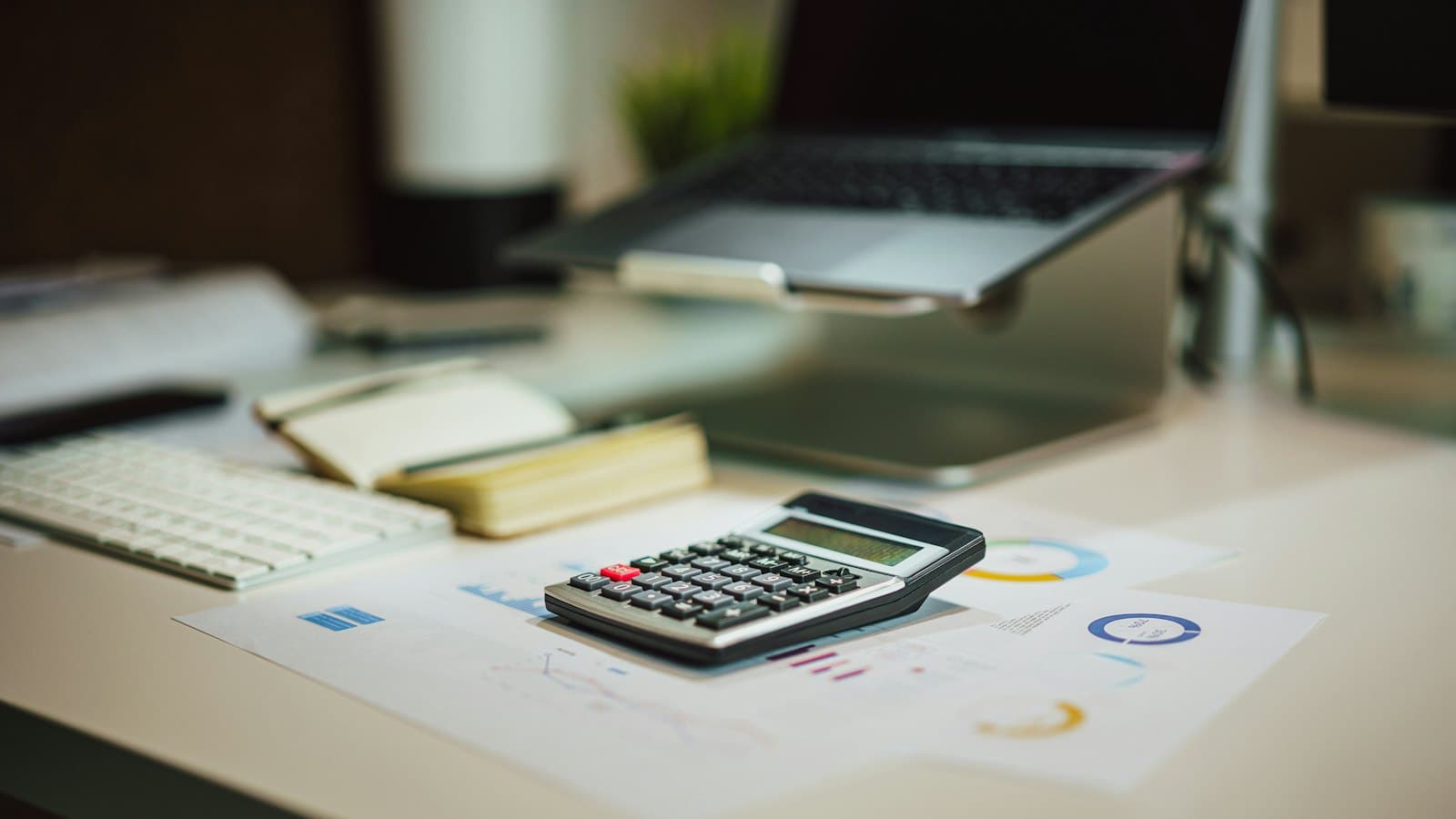 A calculator on printed charts in front of a laptop on a home desk