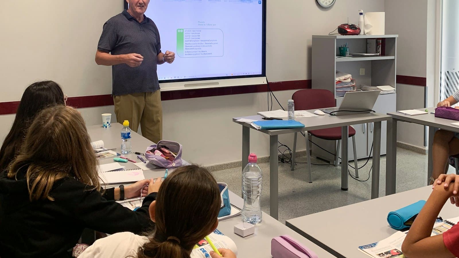 Teacher standing in front of a digital screen while students listen in a classroom