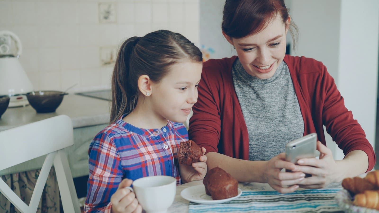 A mother and her daughter sitting together at home, looking at a phone