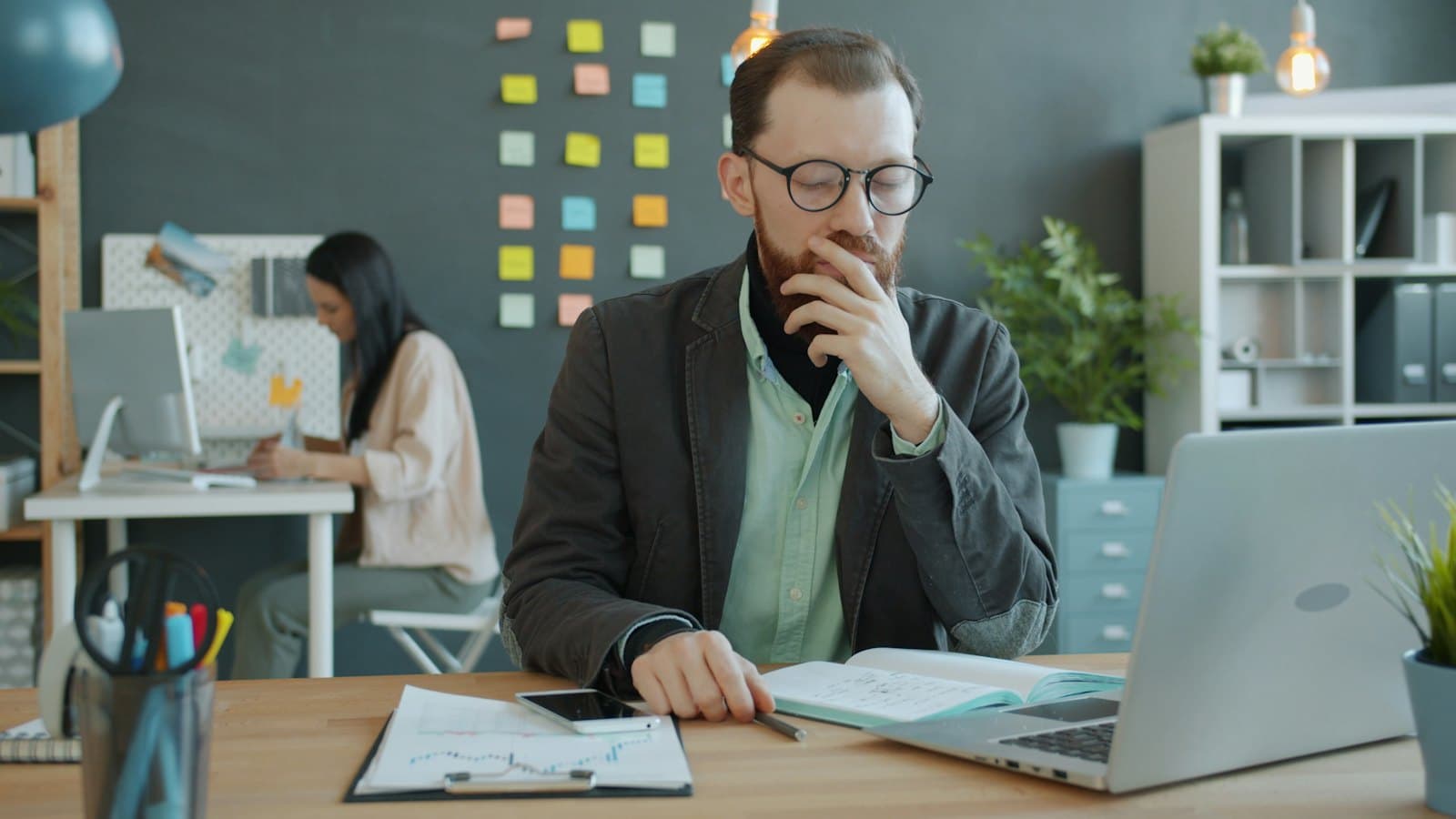 Bearded man in glasses thinking over his notes at an office desk