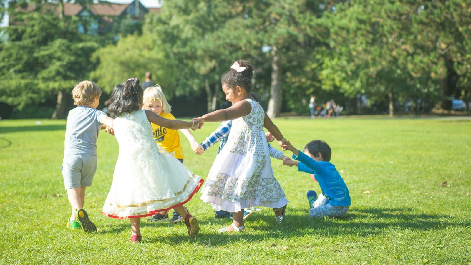 Group of children holding hands in a circle on a sunny park lawn