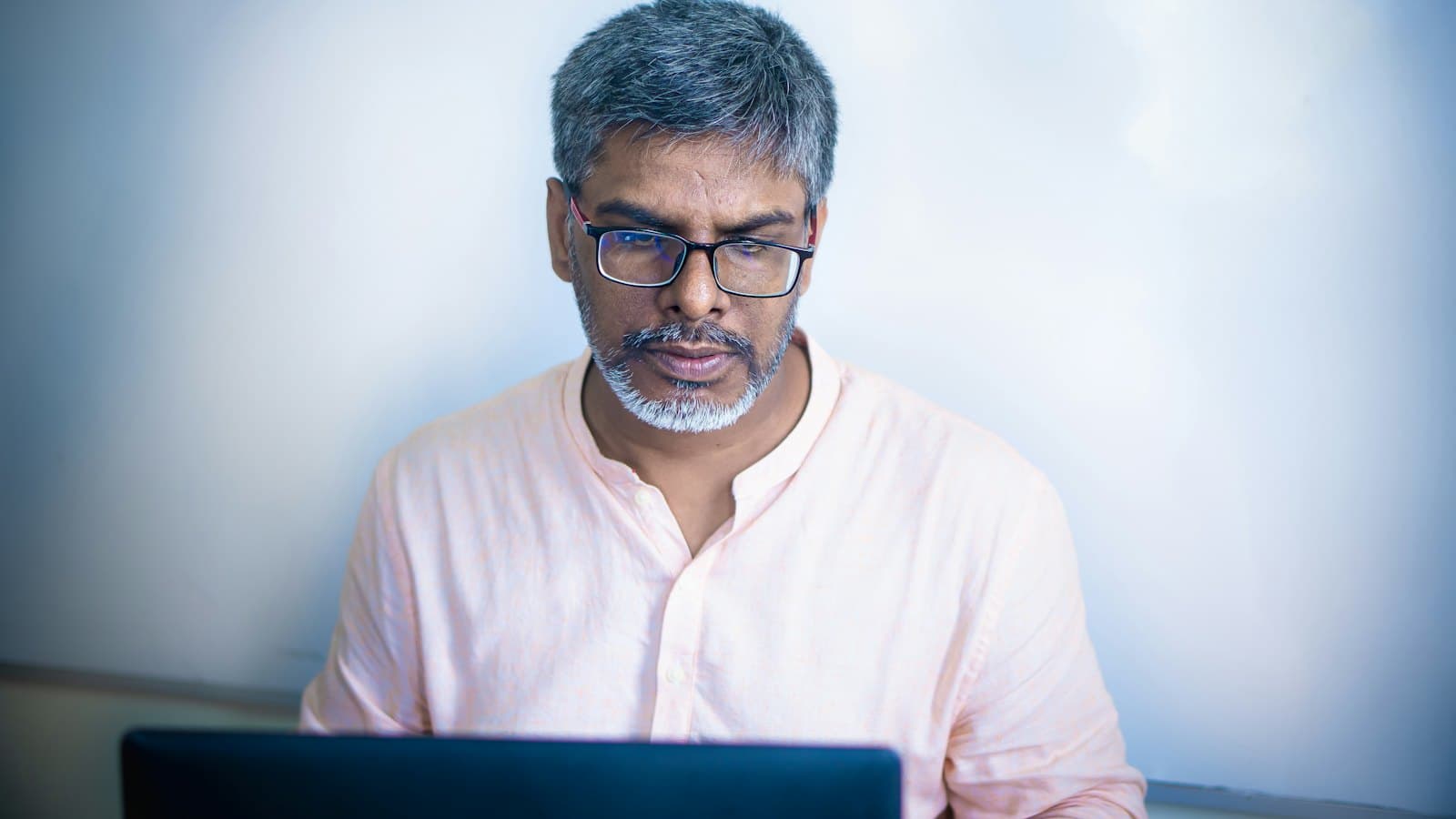 A grey-haired man in glasses concentrating on his laptop at work