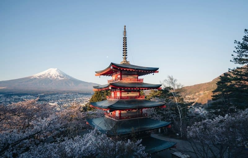 A red five-storey pagoda with snow-capped Mount Fuji behind it