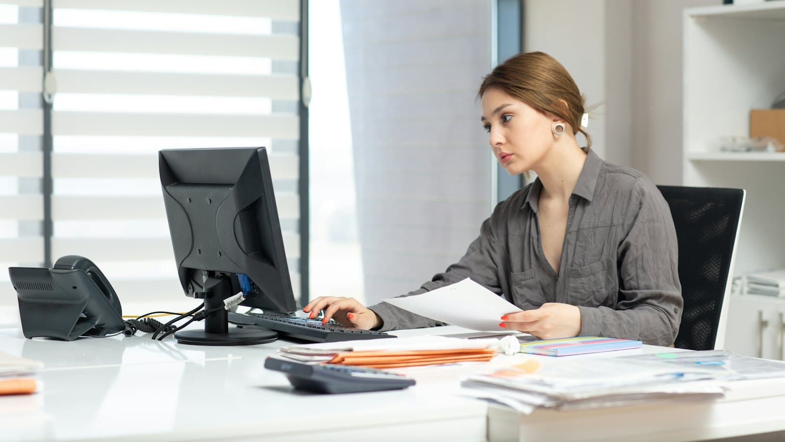 Young woman working through documents and figures at a computer in a bright office
