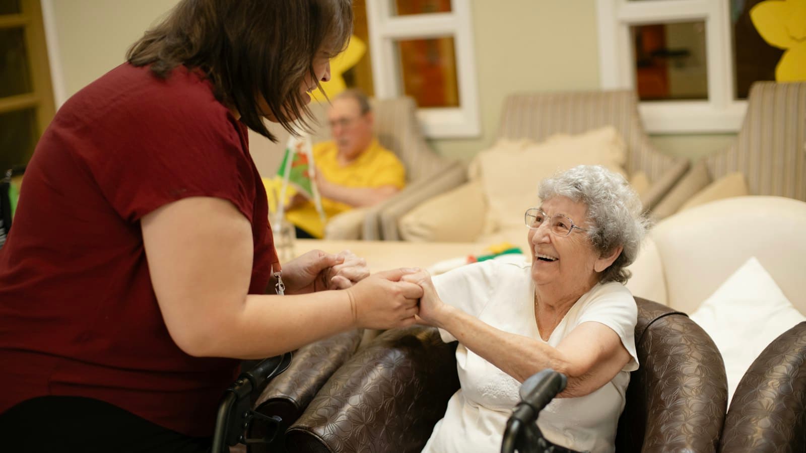 Care worker holding hands with a smiling elderly woman in a care home lounge