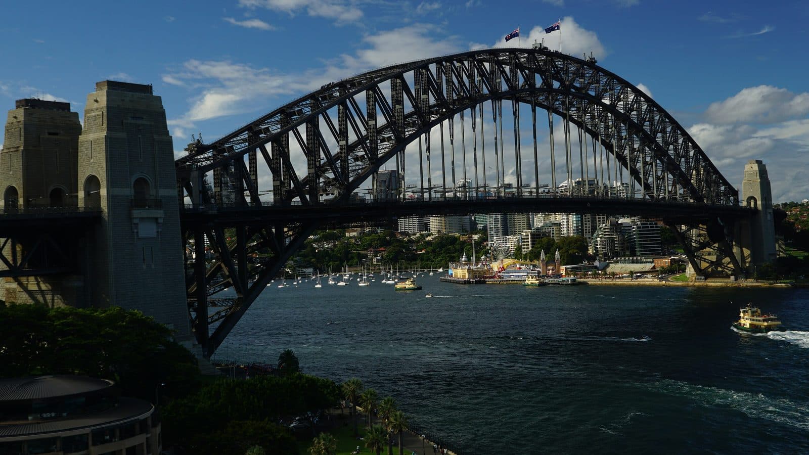 The Sydney Harbour Bridge on a sunny day, with ferries crossing the harbour and the city skyline behind