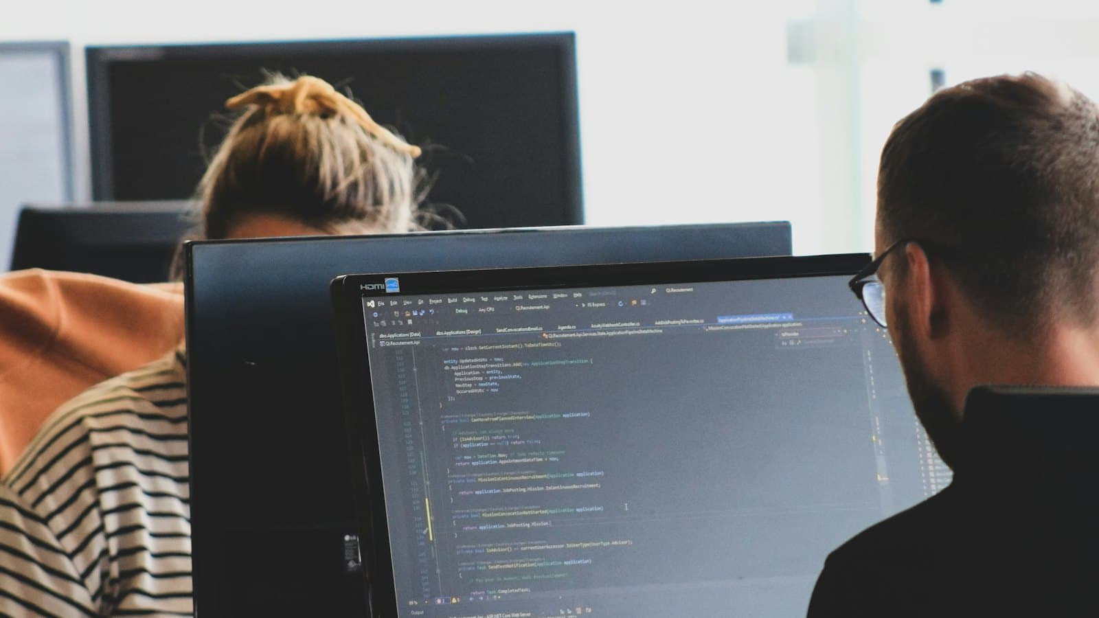 Two software developers reviewing code on monitors in a bright office