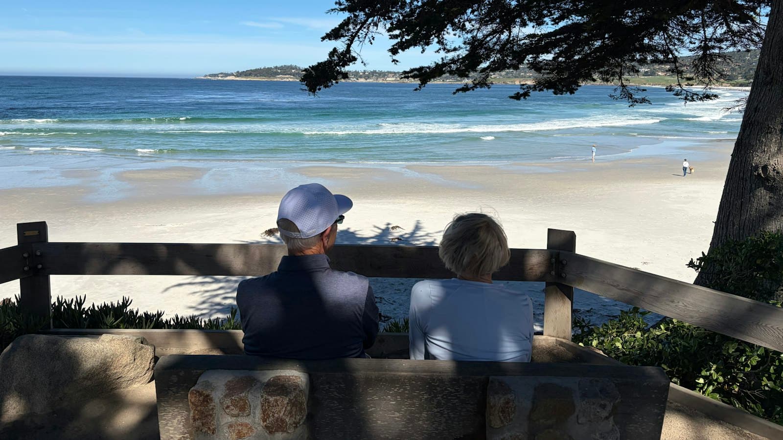 Two people sitting on a bench looking out over a quiet beach
