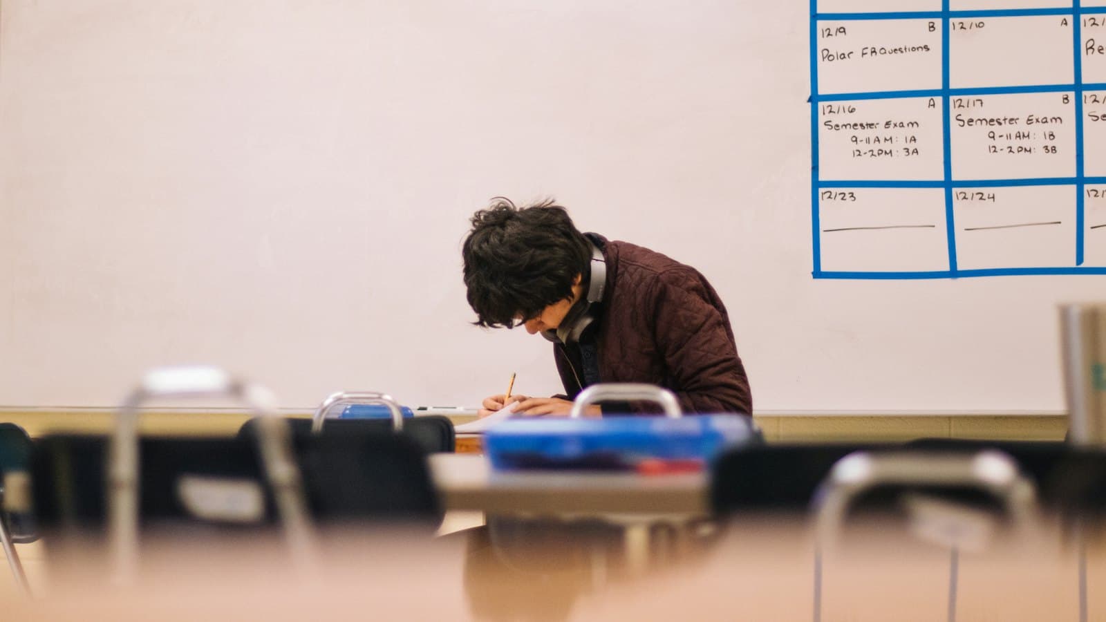 Student writing answers on paper at a desk in a classroom