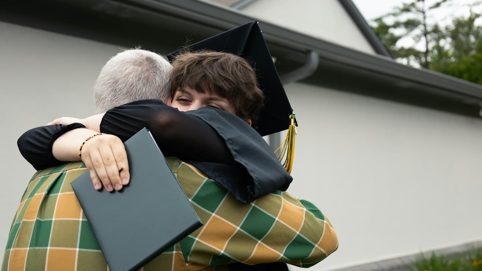 Young graduate in cap and gown hugging a family member outdoors