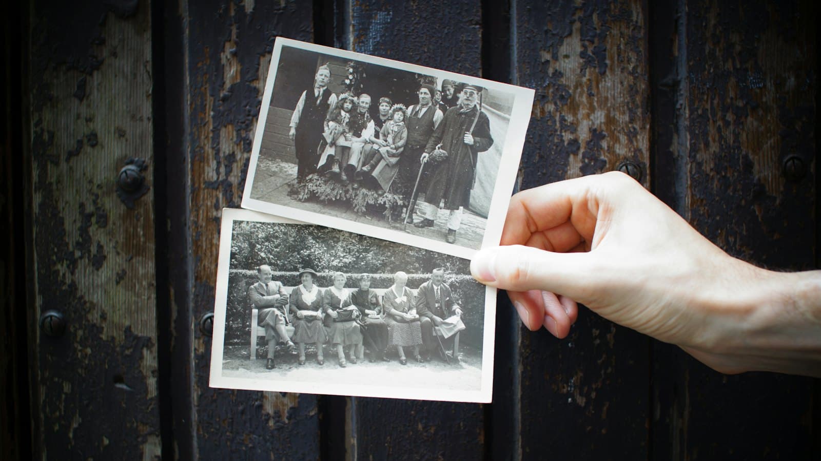 A hand holding two old black and white family photographs against a dark wooden door