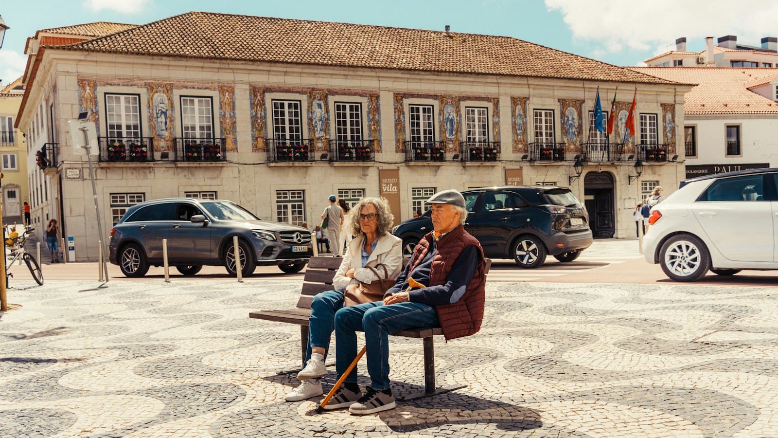 Older couple resting on a bench in a sunny Portuguese town square
