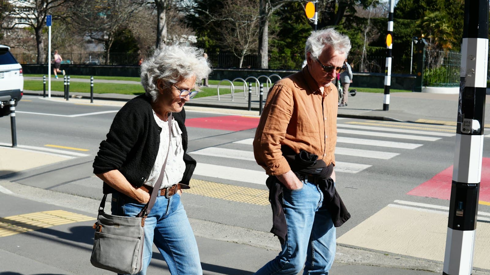 An older woman and man walking across a city crosswalk on a sunny day