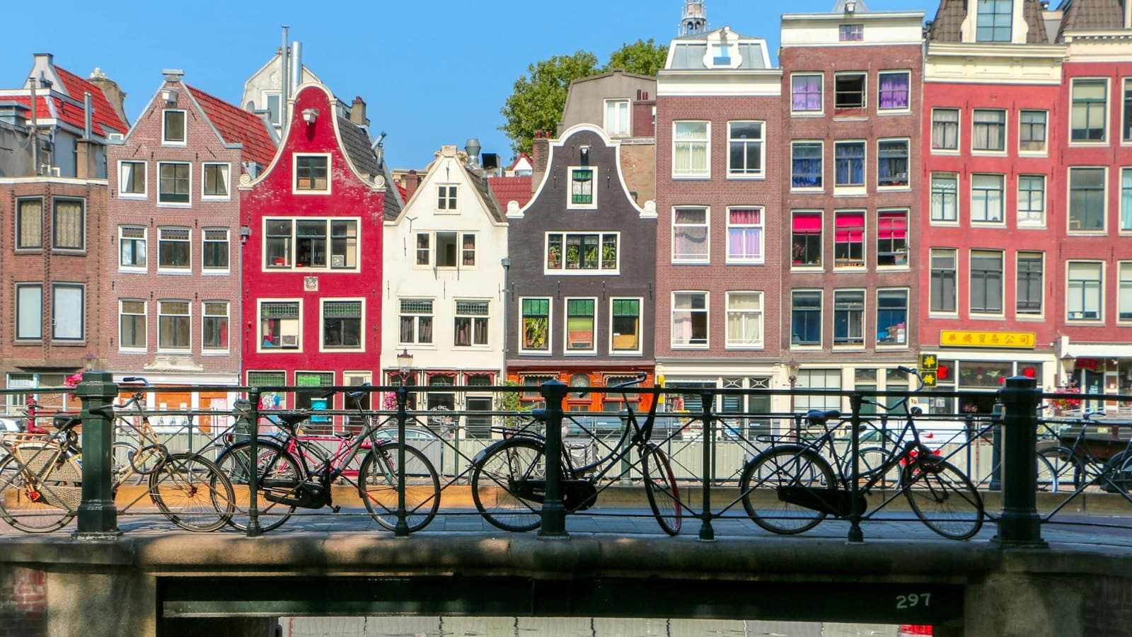 Bicycles parked on a bridge over an Amsterdam canal lined with historic houses