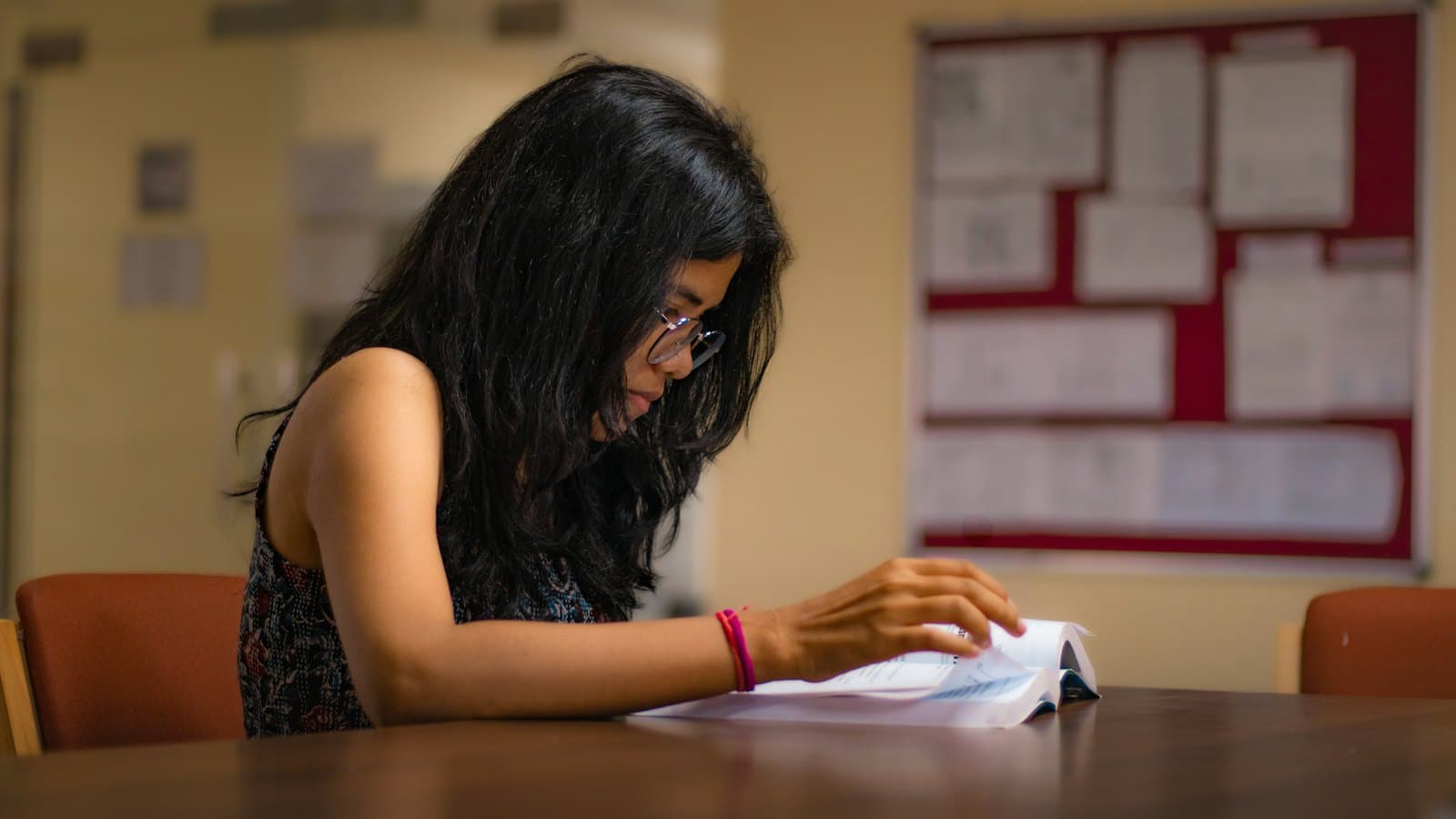 Young woman reading a booklet at a table in a quiet study room