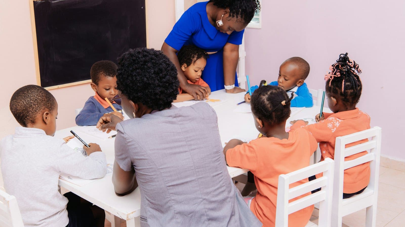 A teacher guiding young children as they draw together at a table