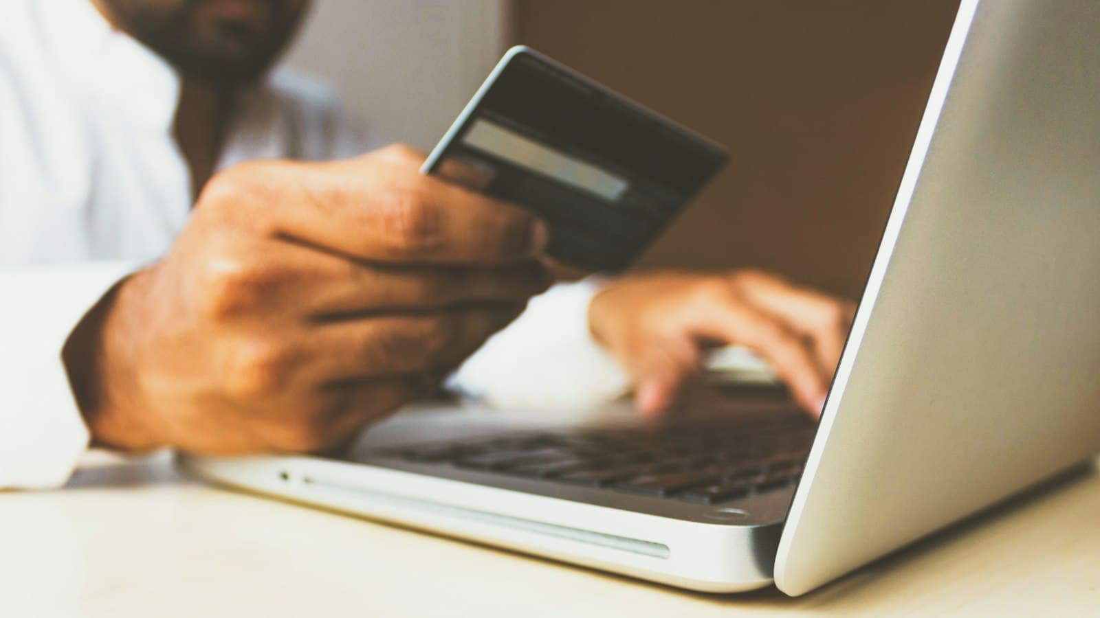 A person holding a bank card in one hand while typing on a laptop with the other