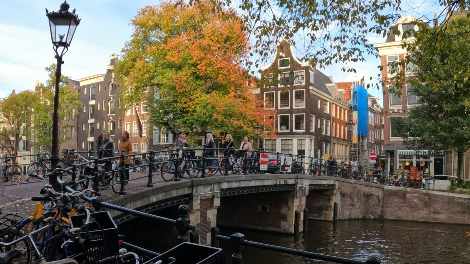 Bicycles locked along a canal bridge lined with autumn trees in Amsterdam