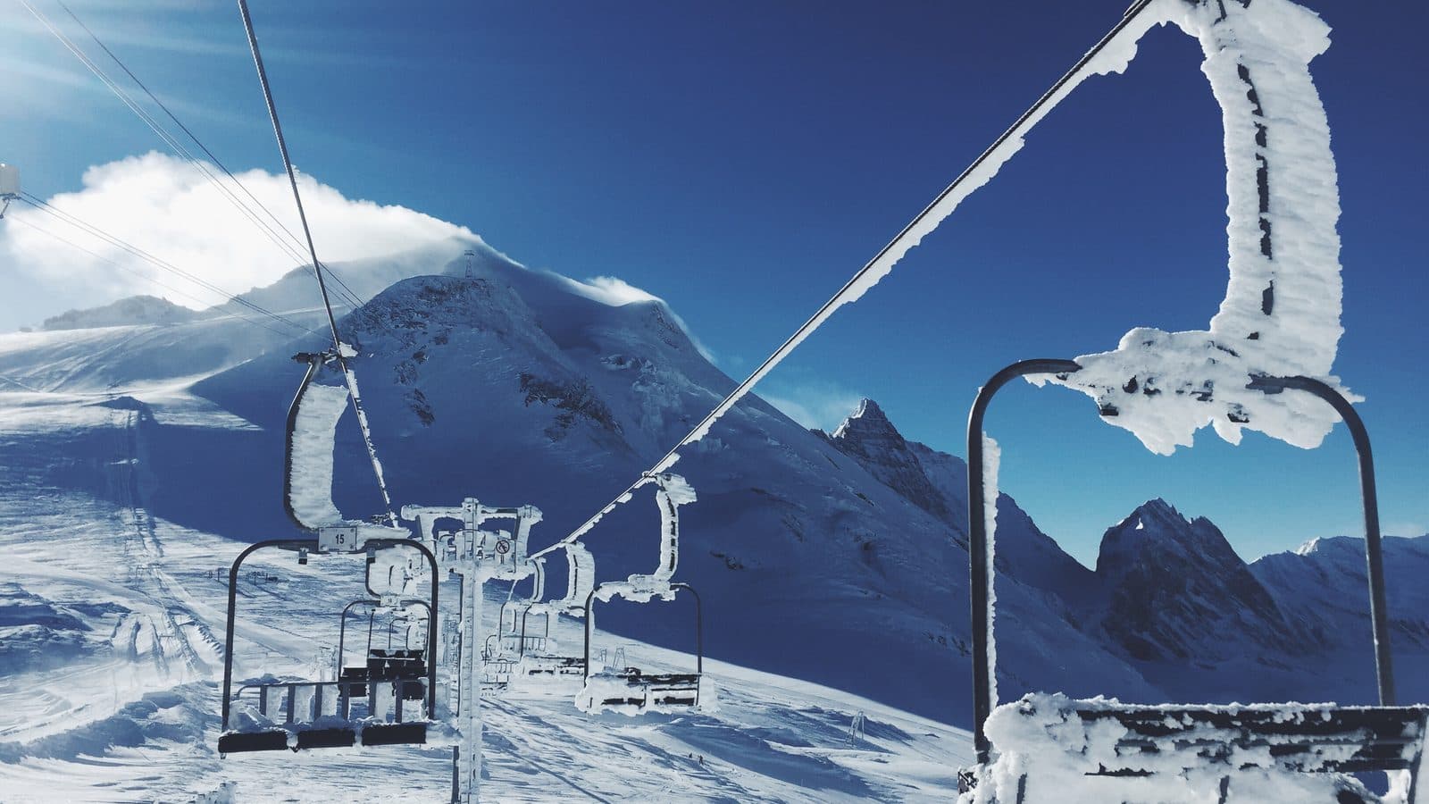 Empty chairlift seats coated in thick frost on a snowy ski slope, with mountains under a deep blue sky